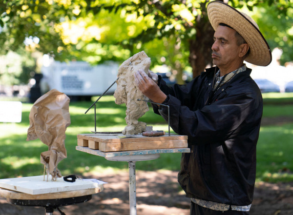 adult man wearing wide brim hat sculpting outside