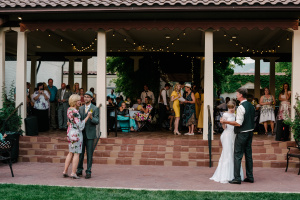 Man in blue suit using his right hand to twirl a woman in wedding dress holding a bouquet of yellow flowers