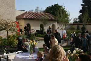 Photo of wedding couple kissing in the center of a group of guests who are holding balloons and smiling